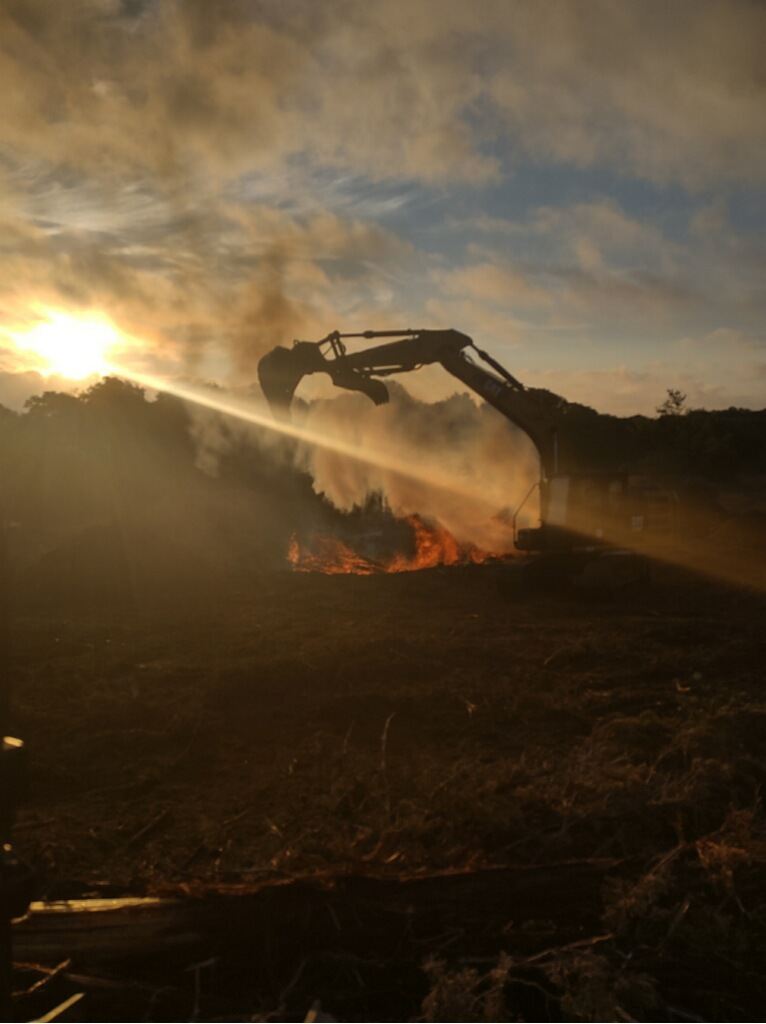 Excavator managing a controlled burn pile at sunset